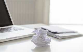 blank laptop screen with crumpled paper on desk