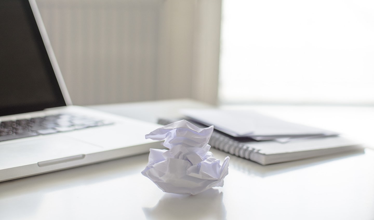 blank laptop screen with crumpled paper on desk